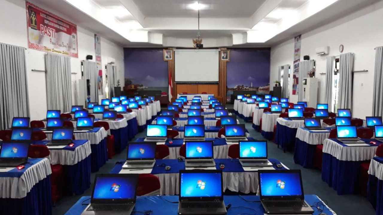 Puluhan unit laptop tertata rapi dalam satu ruangan — ilustrasi skala armada perangkat yang dipantau lewat dashboard manajemen aset IT perusahaan
